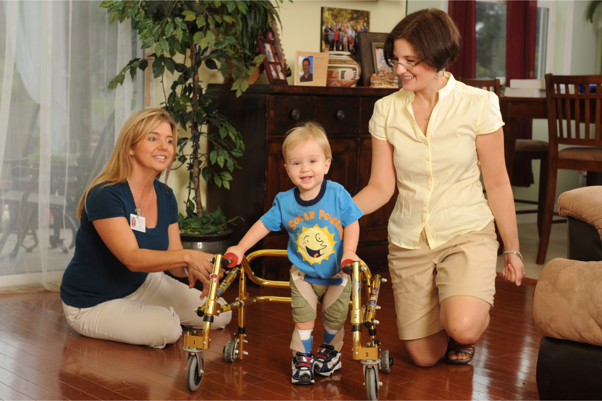 El proveedor de servicios de intervención temprana y la madre observan cómo el niño pequeño camina con el andador