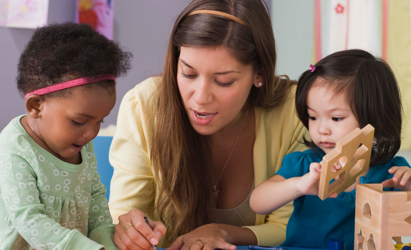 Un proveedor de servicios de intervención temprana trabajando con dos niñas pequeñas mientras colorean y juegan con bloques de aprendizaje