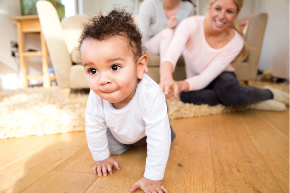 Baby crawling on the floor with mother smiling in background